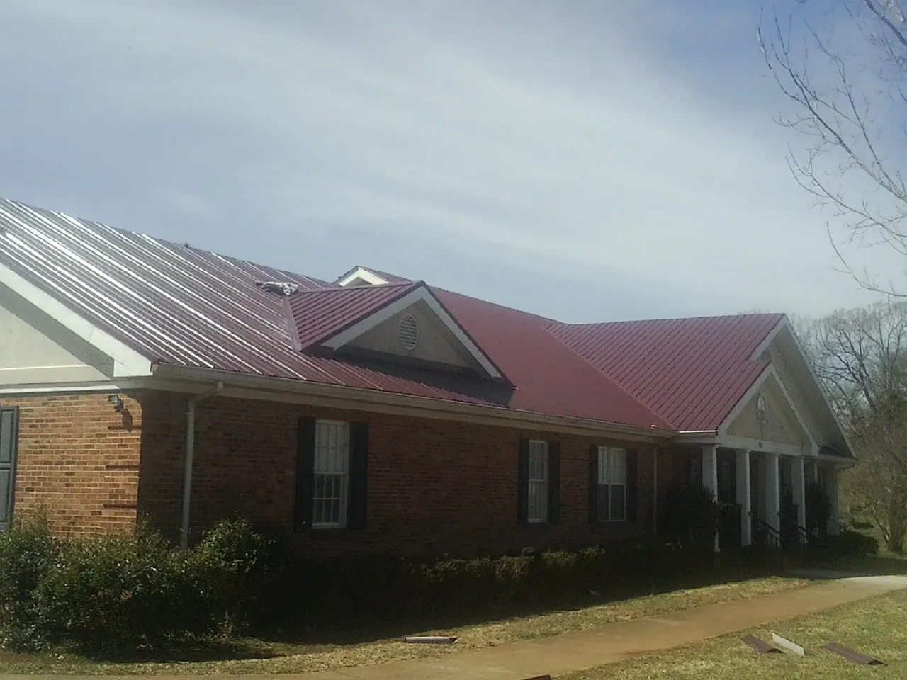Red metal roof with gabled entries on a long brick building, from a Hail Damage Roof Repair job in Tuppers Plains