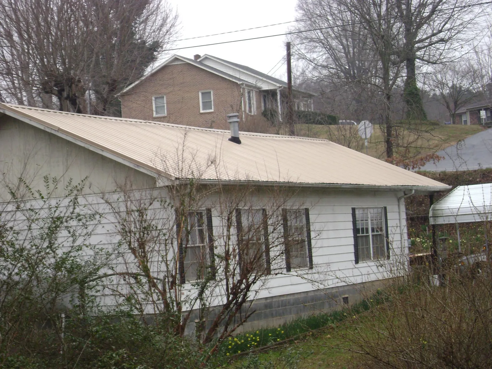 Tan metal roof on a white sided house set into a hillside — Commercial Roofing by Roofing Brothers in Tuppers Plains